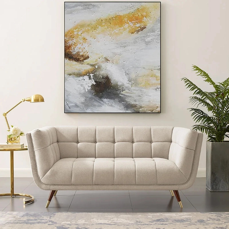 beige fabric sofa with soft curved arms, square cushion details and raised wooden legs — angled view showing the full shap...