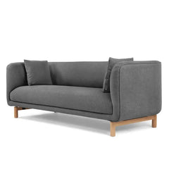 curved fabric sofa with soft wraparound arms, deep cushioning and raised wooden legs — wide room view showing the complete...