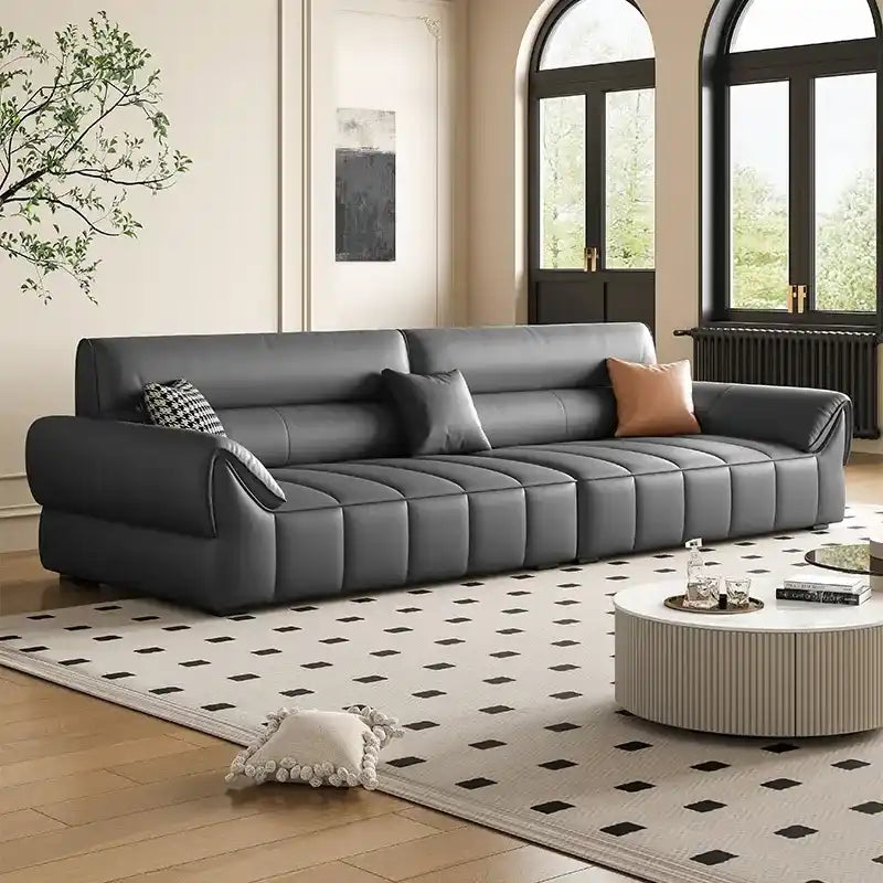 wide leatherette sofa with deep square cushioning and a low relaxed shape — front view in a bright living room