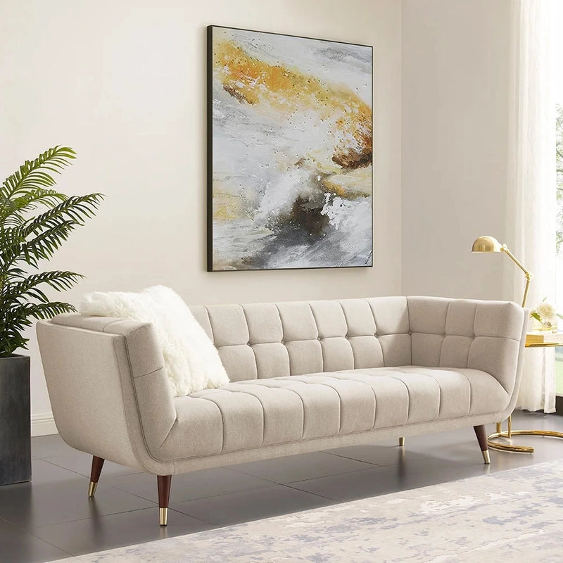 beige fabric sofa with soft curved arms, square cushion details and raised wooden legs — front view in a bright living room