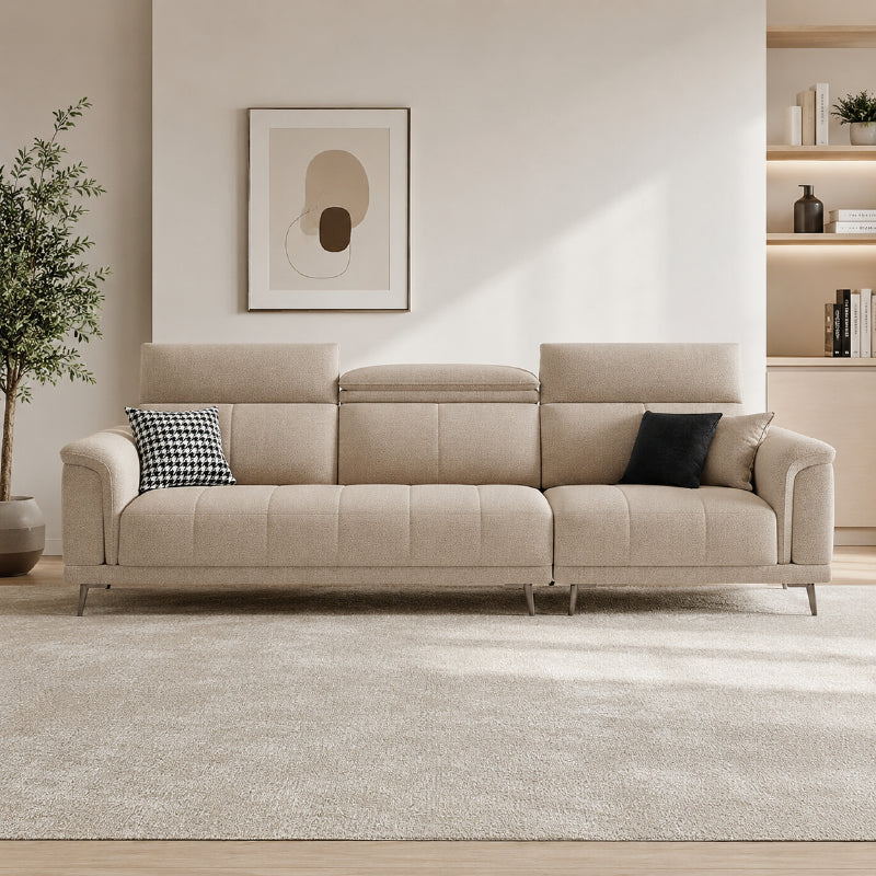 beige l shape sofa with adjustable head support, rounded arms and slim raised legs — angled view showing the full shape an...
