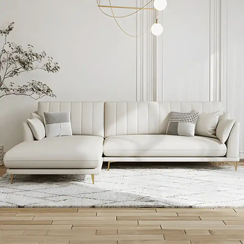 soft cream corner sofa with deep cushions, vertical back details and slim gold finish legs — angled view showing the full...