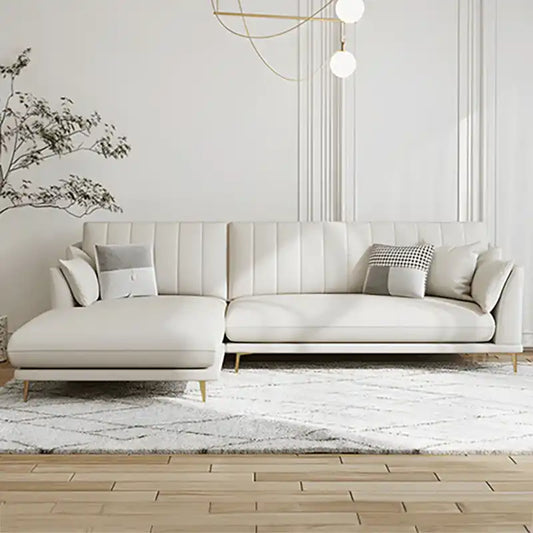 soft cream corner sofa with deep cushions, vertical back details and slim gold finish legs — angled view showing the full...