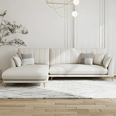 soft cream corner sofa with deep cushions, vertical back details and slim gold finish legs — angled view showing the full...