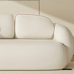 soft curved fabric sofa with cloud like cushions, wraparound arms and a low grounded base — side angle showing the arms an...