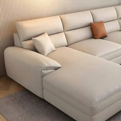 beige l shape leatherette sofa with deep seating, high back cushions and wide padded arms — side angle showing the arms an...