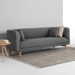 curved fabric sofa with soft wraparound arms, deep cushioning and raised wooden legs — close view showing the cushion and...